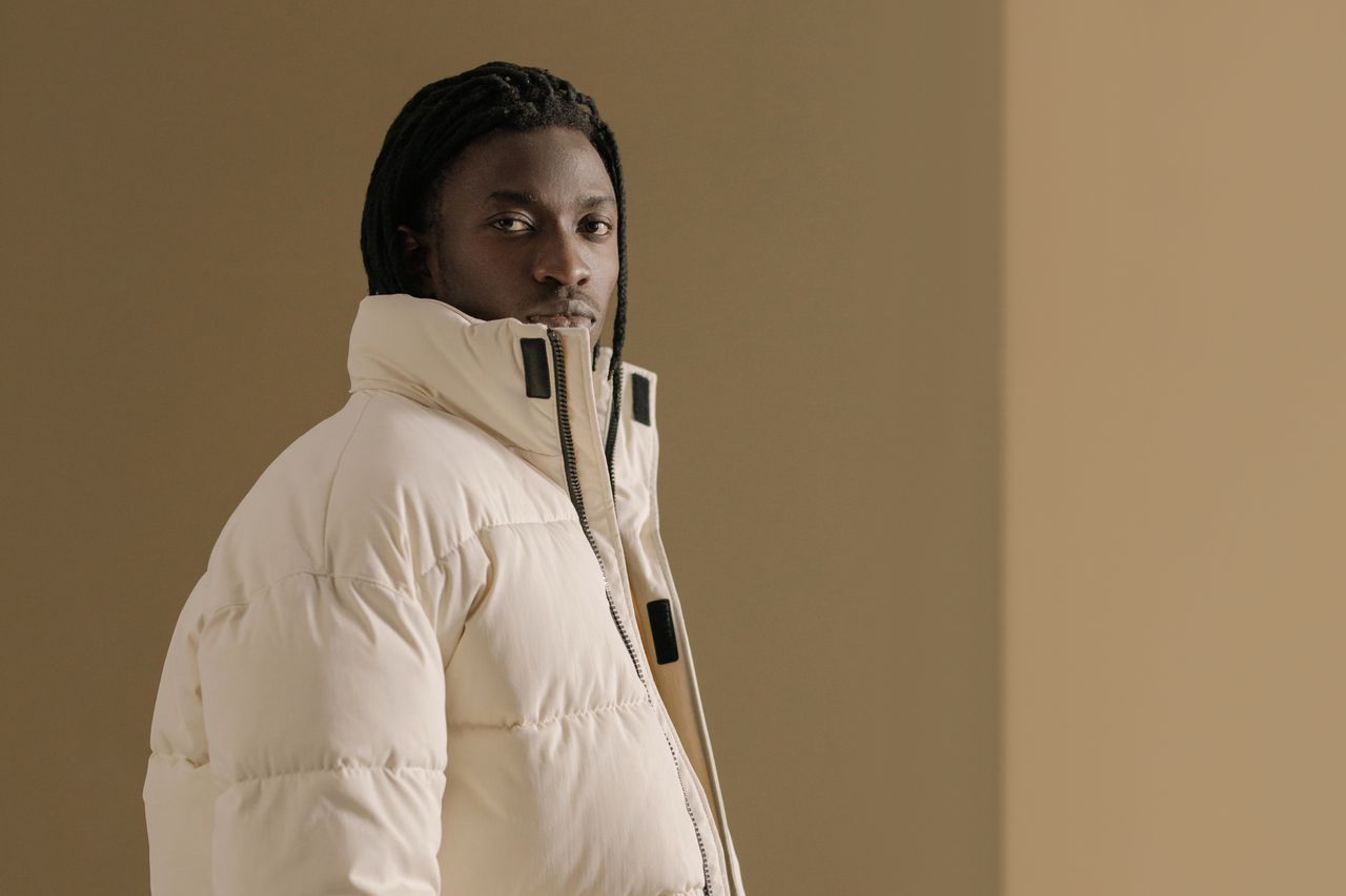 Portrait of a man in a beige winter coat with a neutral background, exuding style and confidence.