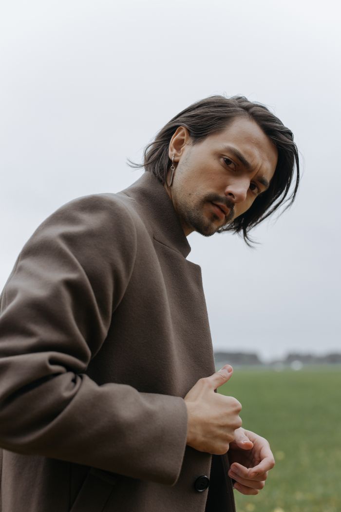 A fashionable man posing with a serious expression in an open field, showcasing modern style.